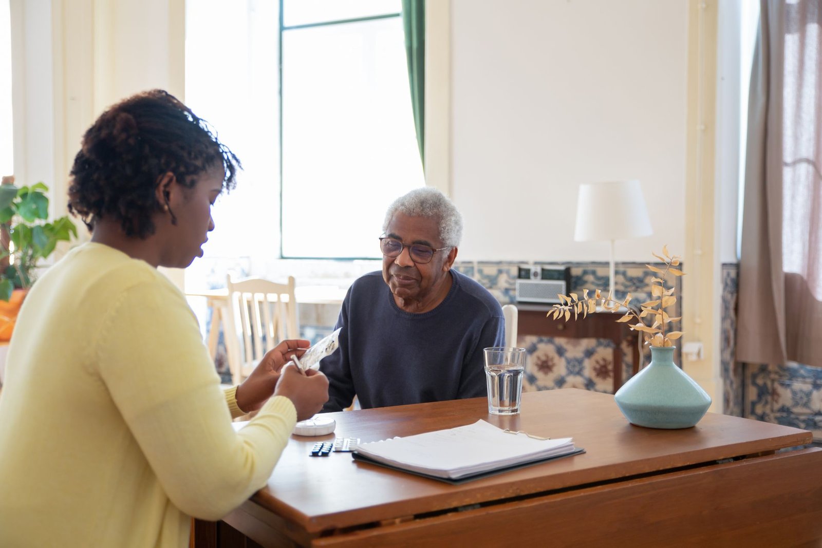 Caregiver preparing medication for an elderly man in his living room
